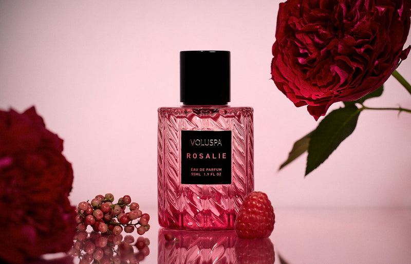Voluspa Rosalie Eau de Parfum bottle surrounded by deep red roses and fresh raspberries against a soft pink background